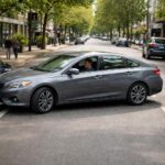 Carro estacionando em paralelo entre dois veículos em uma rua urbana movimentada com pedestres ao redor.